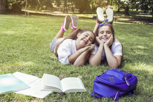 two-schoolgirls-lying-grass-with-heads-propped-hands-smiling